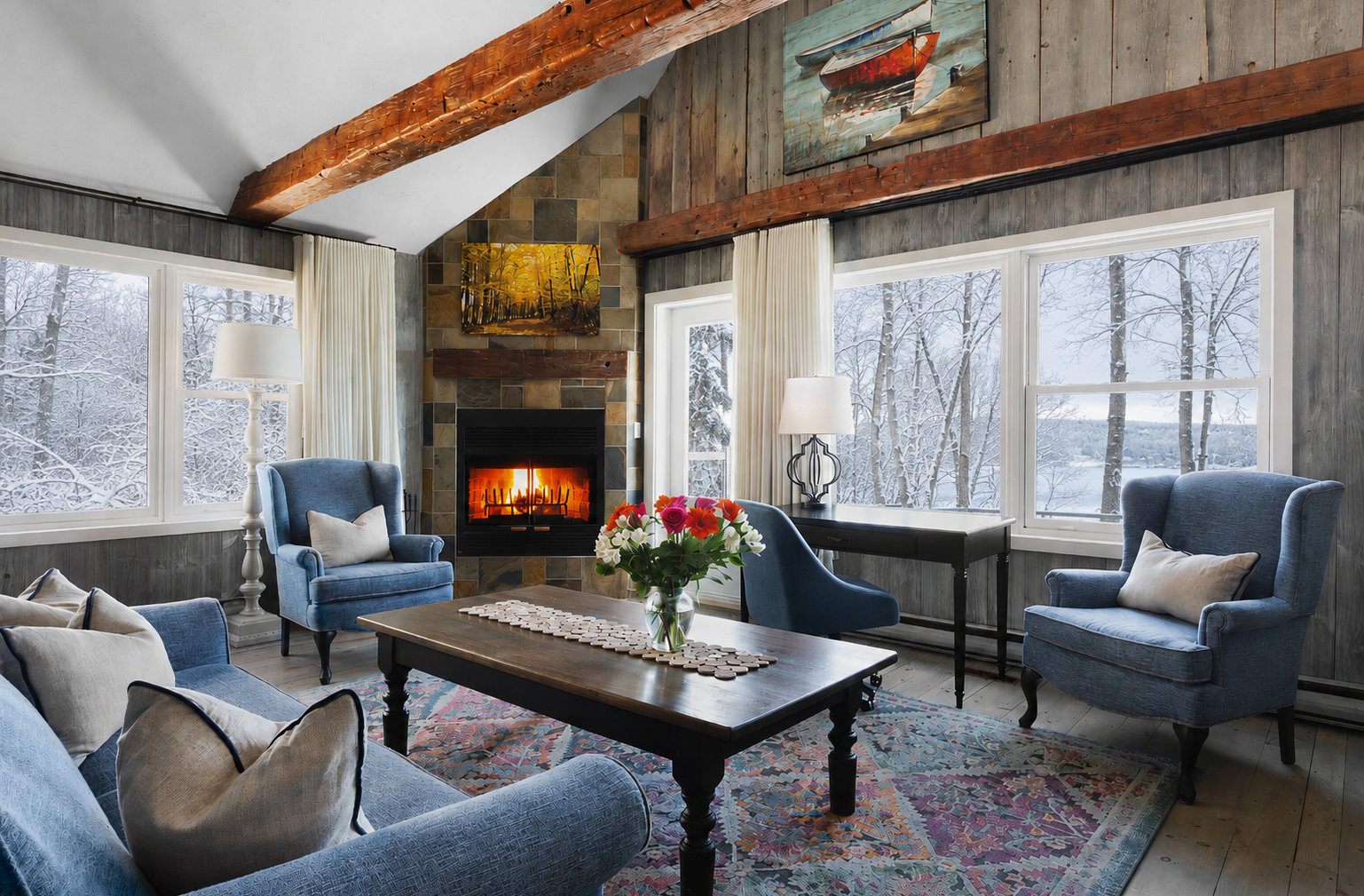 Coin salon chaleureux avec poutres apparentes, lambris rustique et foyer en pierre. De grandes fenêtres offrent une belle vue sur les arbres et le lac, baignant la pièce de lumière naturelle. Des fauteuils confortables et des finitions chaleureuses créent une atmosphère invitante, idéale pour se détendre au coin du feu.
