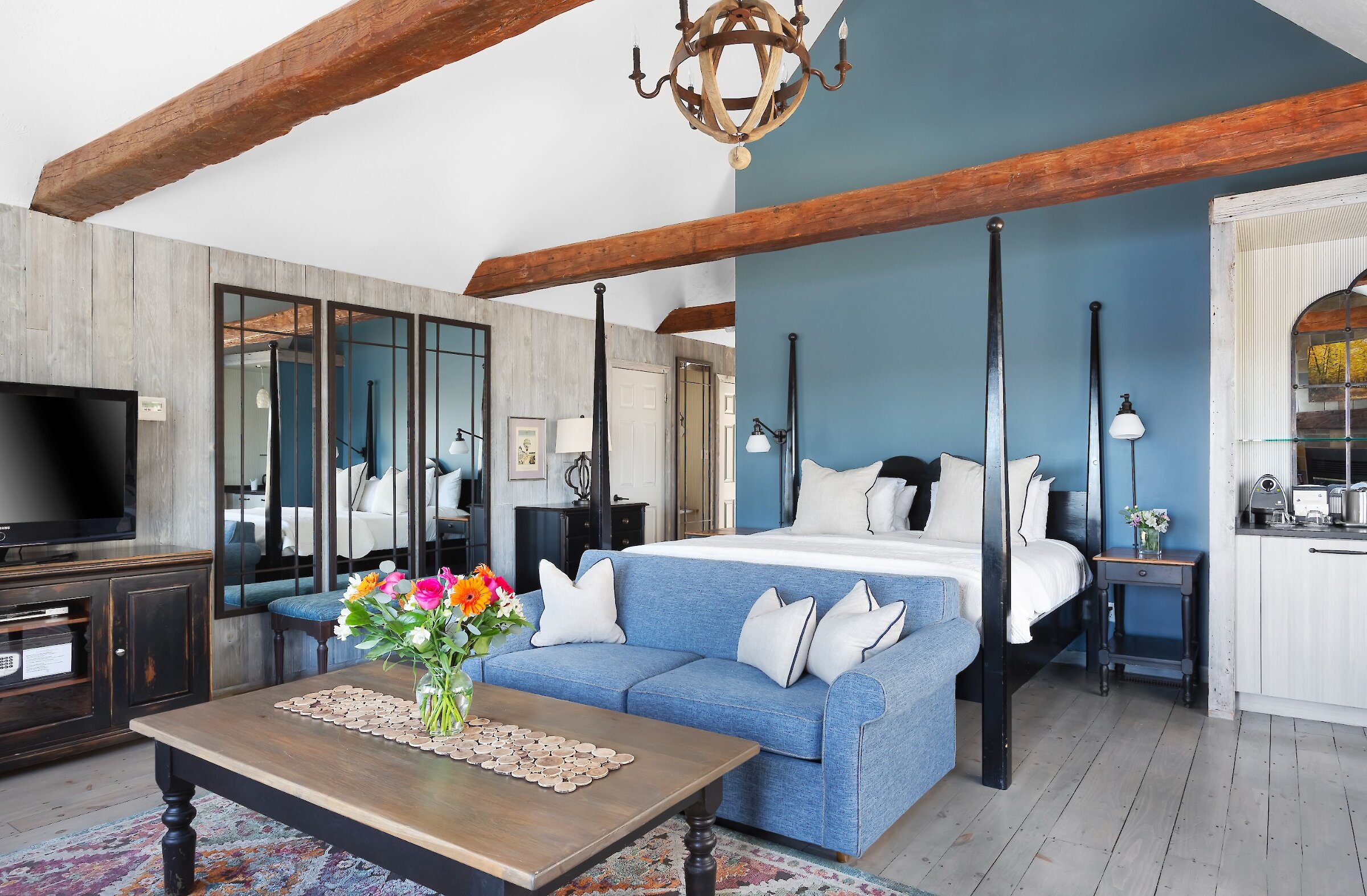 Chambre spacieuse de style pavillon avec poutres apparentes et plafond cathédrale. Elle comprend un lit king à baldaquin, un coin salon confortable et un mobilier élégant aux tons doux et naturels. Une atmosphère chaleureuse et raffinée, alliant charme rustique et confort contemporain.