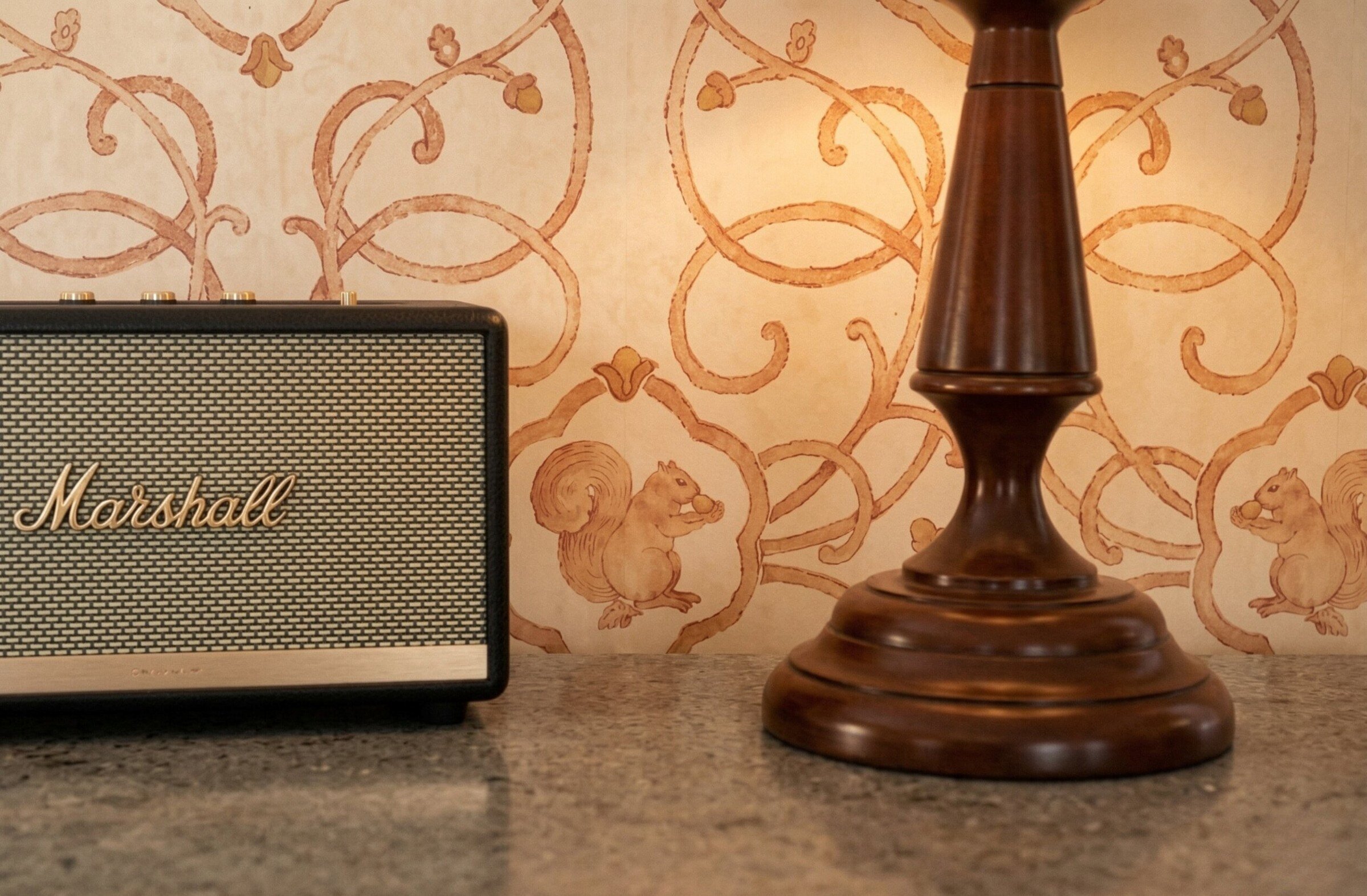 Haut-parleur Marshall et lampe en bois sur une table avec papier peint à motifs.