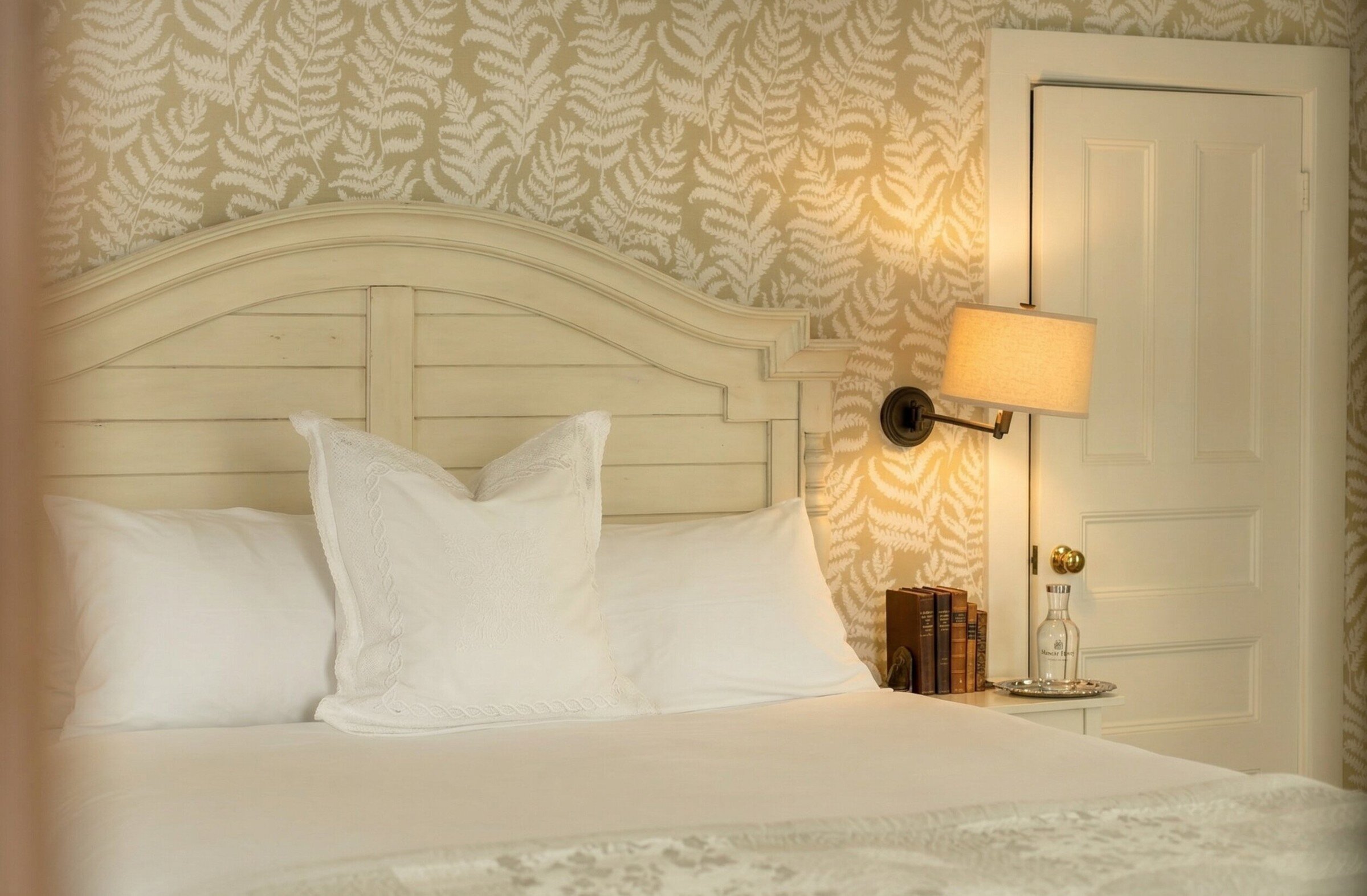 Lit avec literie blanche, tête de lit, lampe et livres.