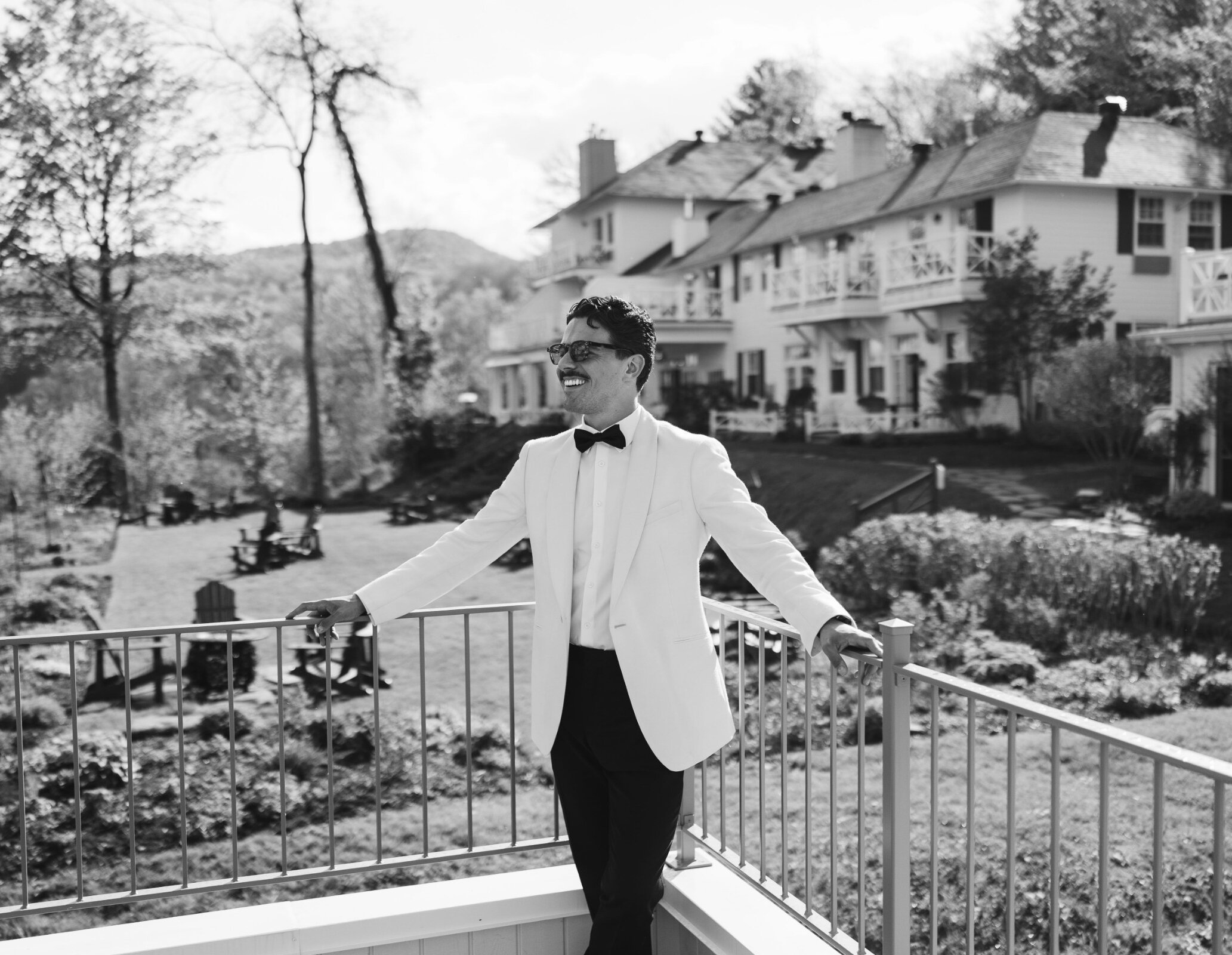 Groom in formal attire standing on a terrace overlooking the gardens.