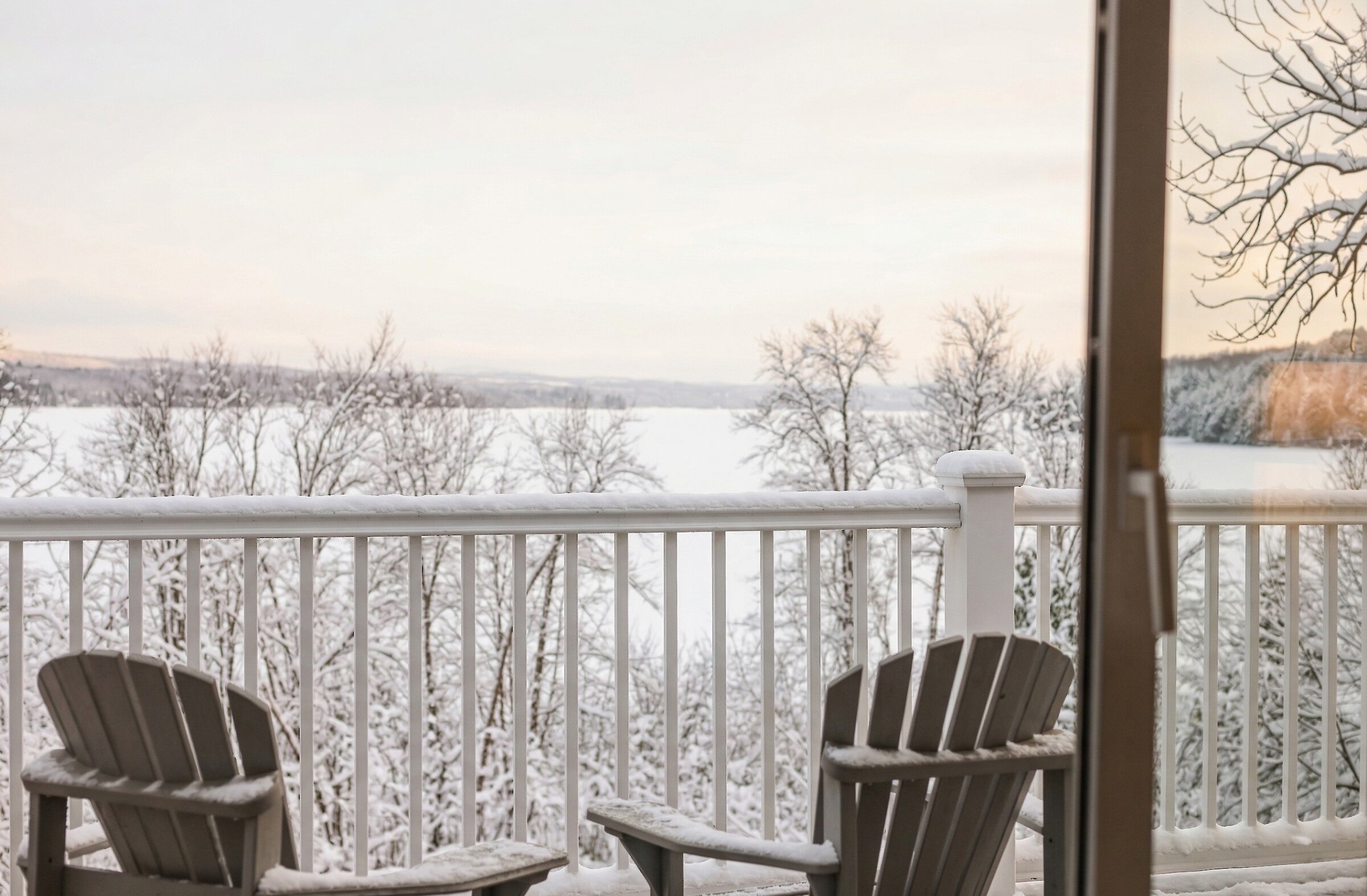 Balcon privé avec deux chaises Adirondack offrant une vue panoramique sur le lac Massawippi et les paysages enneigés environnants.