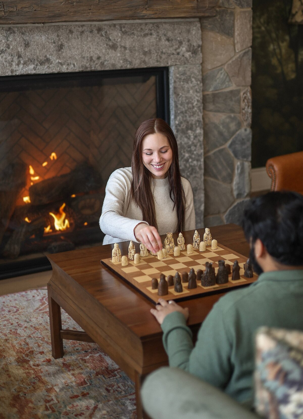 Two people playing chess by the fireplace