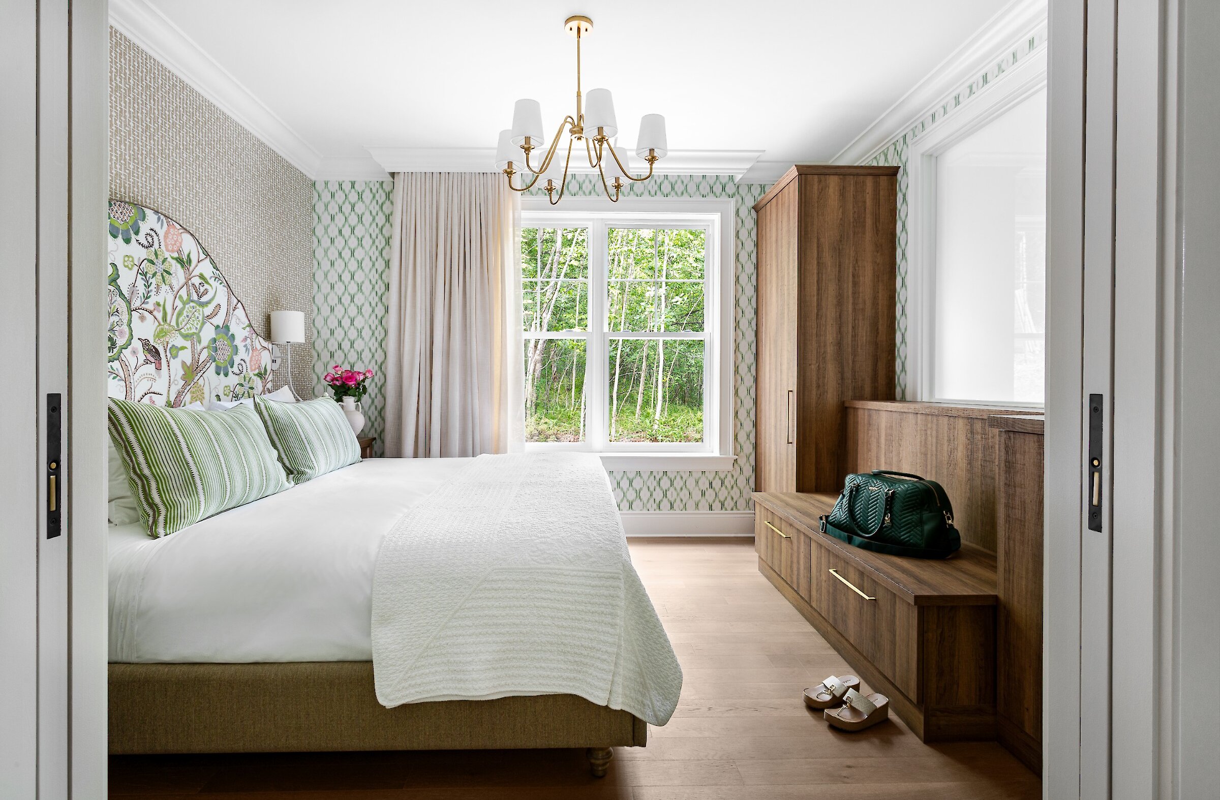 Chambre lumineuse aux tons naturels, rehaussée de motifs botaniques et d’élégantes boiseries, avec vue sur la forêt environnante.