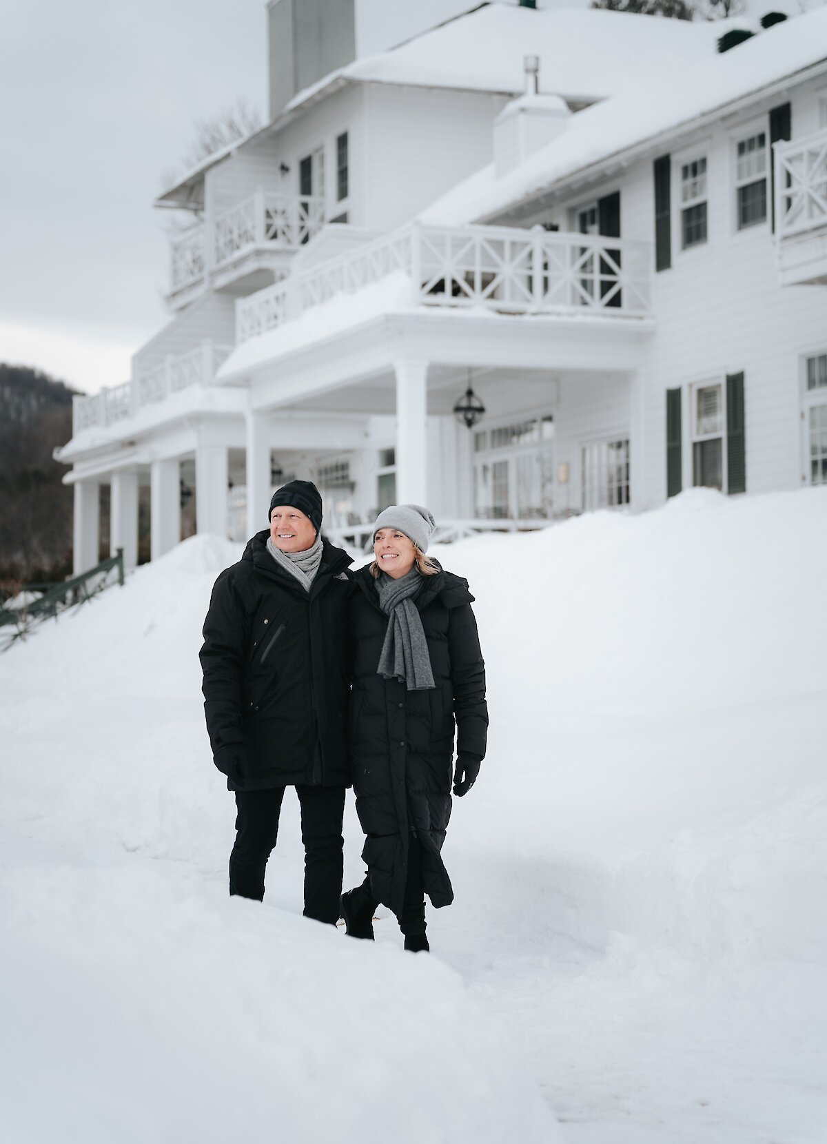 A couple walking in the snow in front of a hotel.