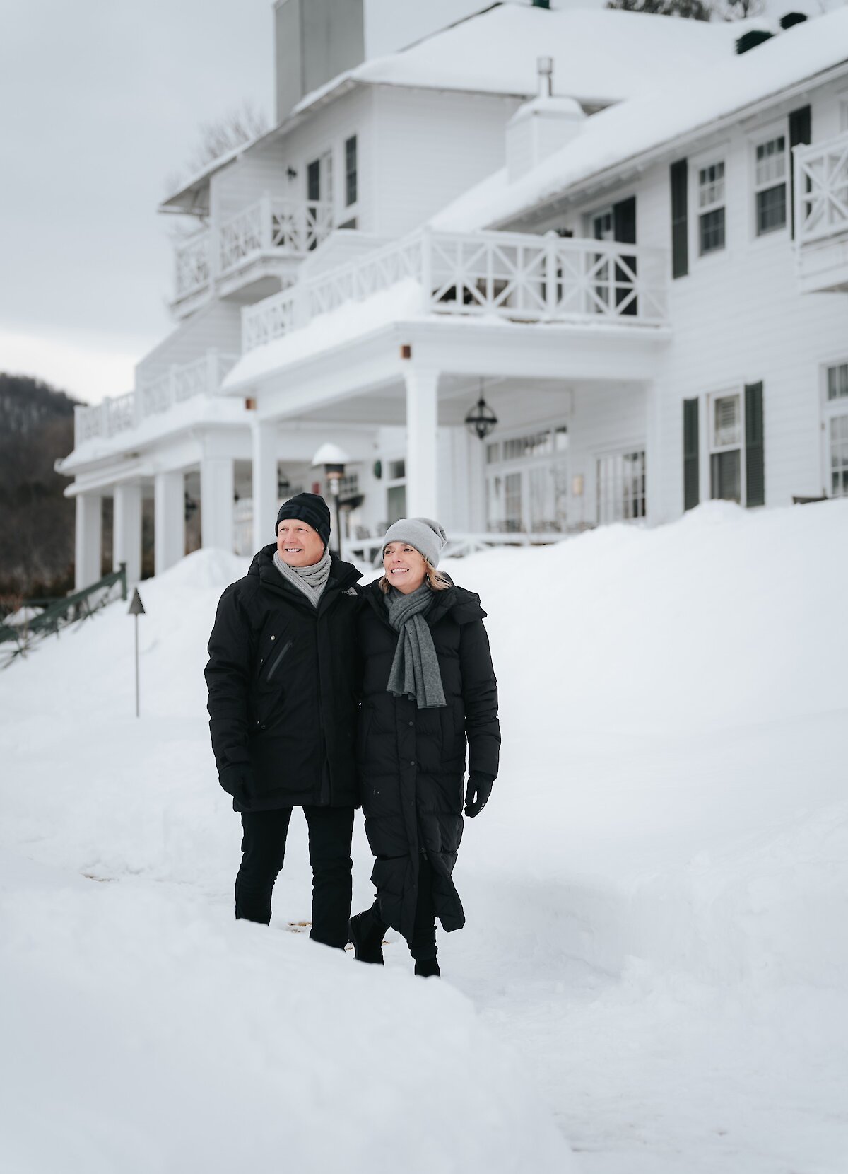 Un couple marche sous la neige devant un hôtel.