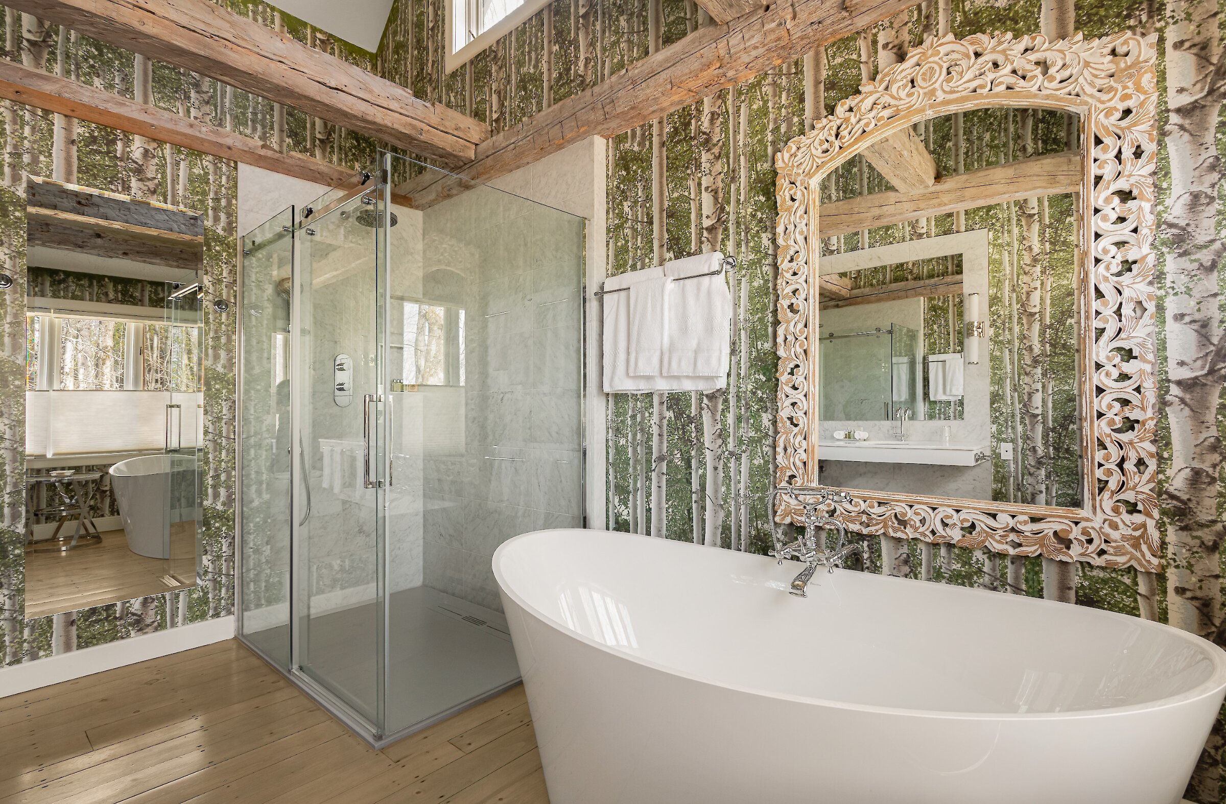Bright bathroom with a freestanding tub, glass shower, exposed beams and forest-inspired décor.