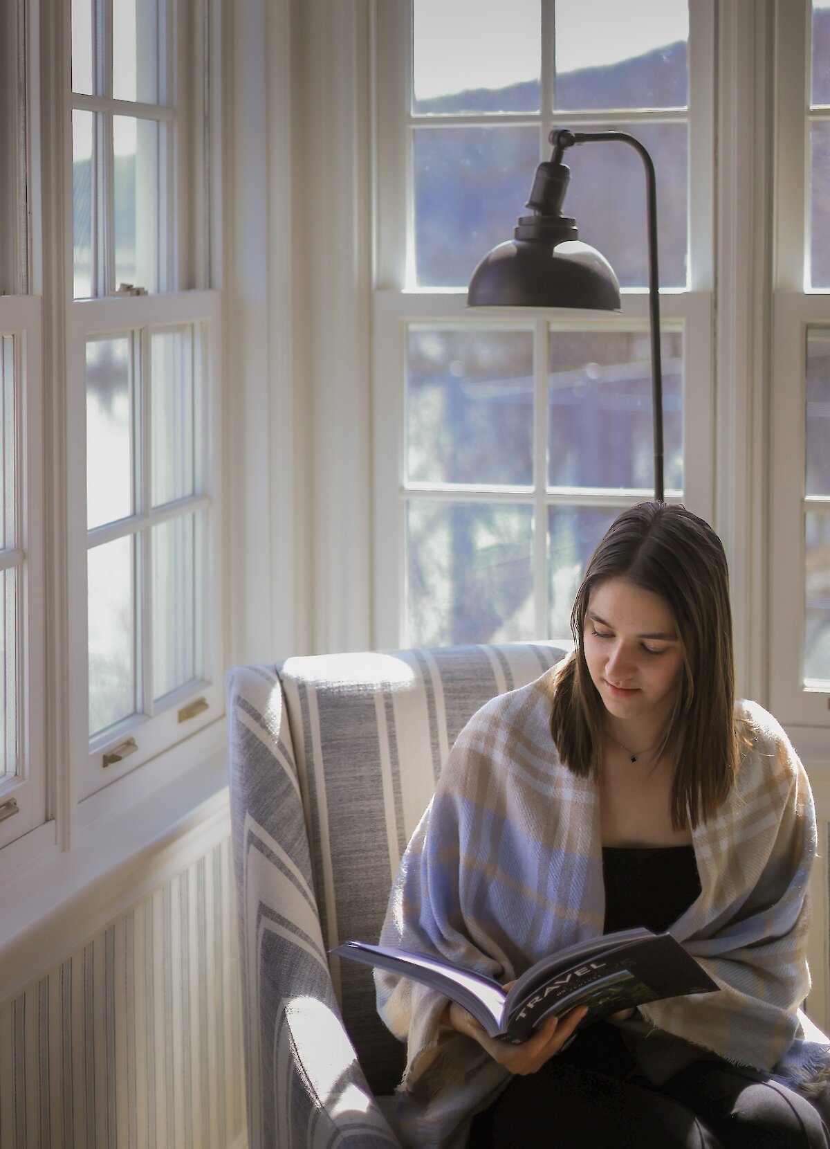 A woman reading a book by the window.