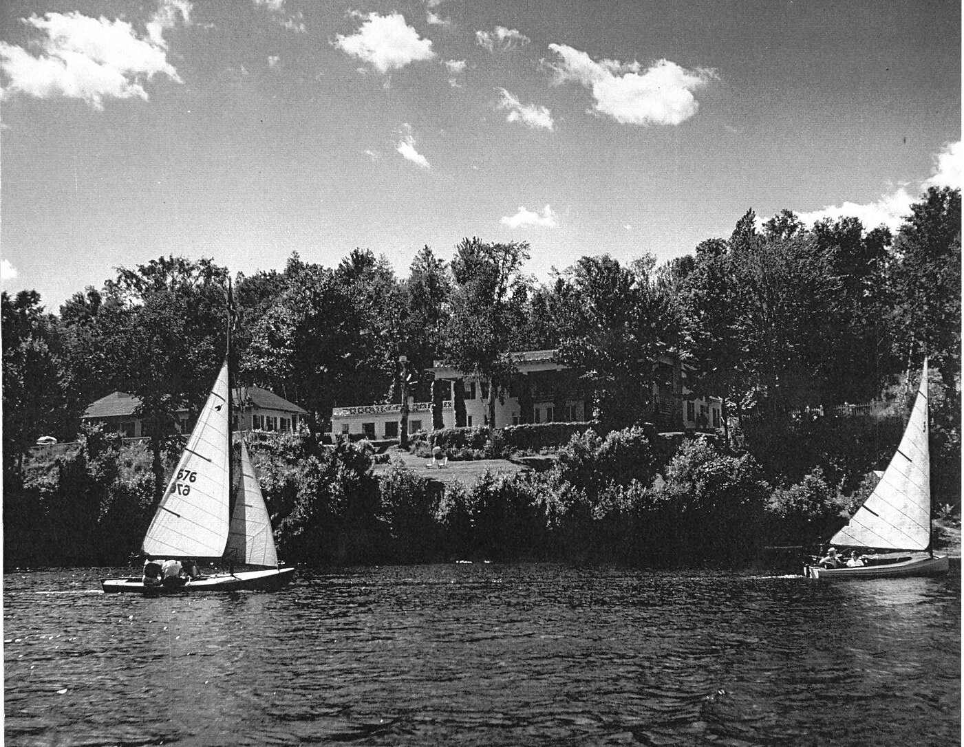 An old photo showing a sailboat on the lake in front of a hotel.