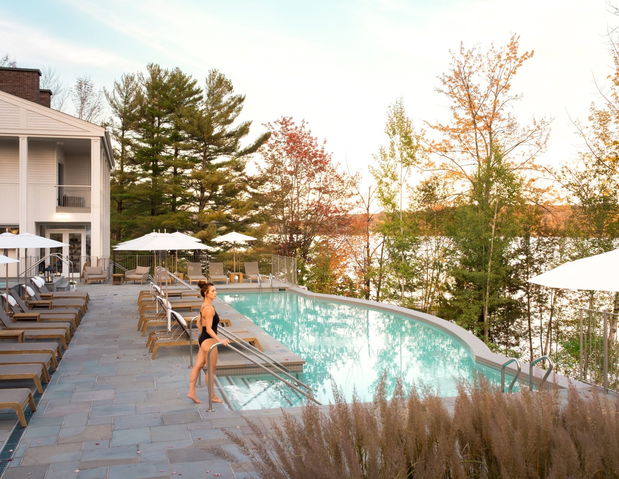 Woman entering the outdoor pool at Manoir Hovey, overlooking Lake Massawippi and surrounded by autumn foliage.