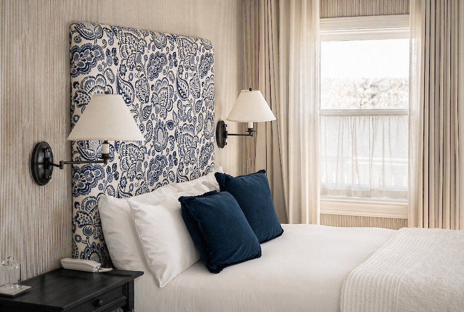 Chambre classique du Manoir Hovey avec tête de lit à motif bleu, literie élégante et lumière naturelle près de la fenêtre