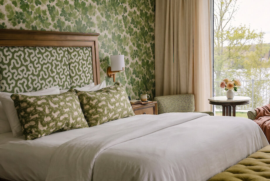 Elegant guest room featuring layered green botanical patterns, warm wood accents, and serene lake views for a refined countryside retreat.
