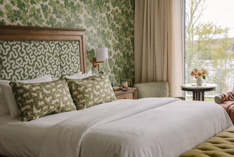 Chambre élégante aux motifs botaniques verts, avec accents de bois chaleureux et vue apaisante sur le lac, offrant une retraite champêtre raffinée.