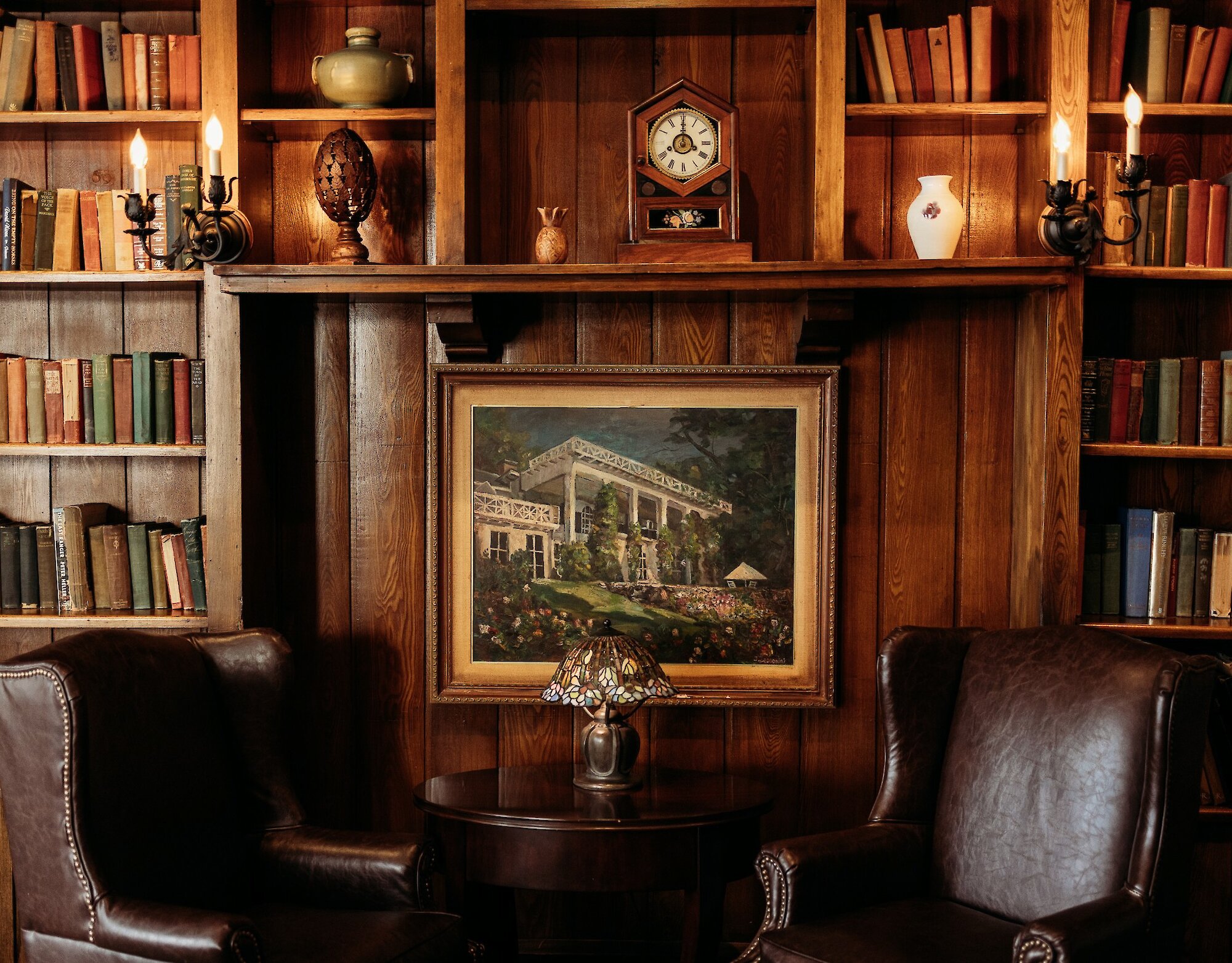 Une bibliothèque chaleureuse aux boiseries élégantes, garnie de livres et baignée d’une lumière douce, avec des fauteuils en cuir et une atmosphère raffinée et intemporelle.