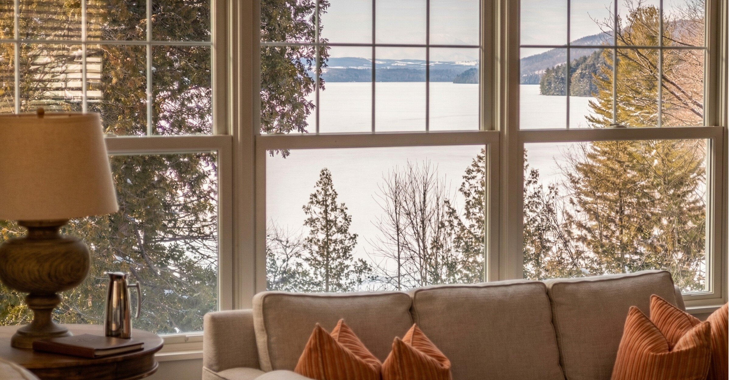 Un espace de vie chaleureux au bord du lac, encadré de vastes fenêtres offrant une vue paisible sur le lac Massawippi et la forêt environnante en hiver.