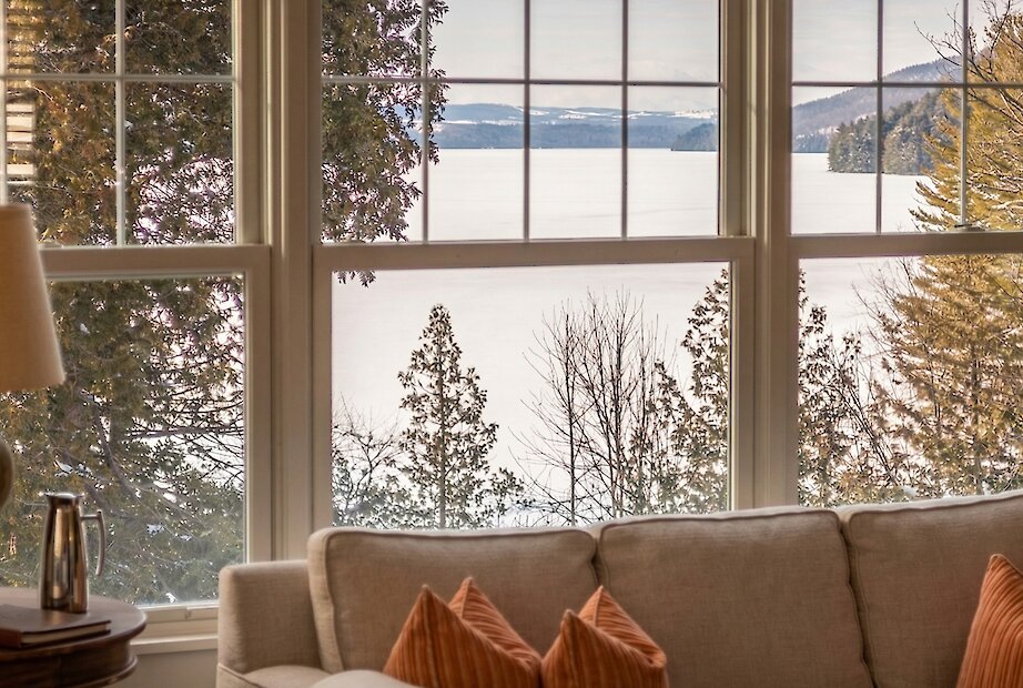 Un espace de vie chaleureux au bord du lac, encadré de vastes fenêtres offrant une vue paisible sur le lac Massawippi et la forêt environnante en hiver.