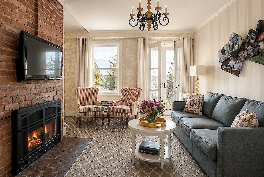 Un salon élégant et chaleureux avec un foyer en brique, une abondante lumière naturelle et une décoration intemporelle offrant une magnifique vue sur le paysage environnant.