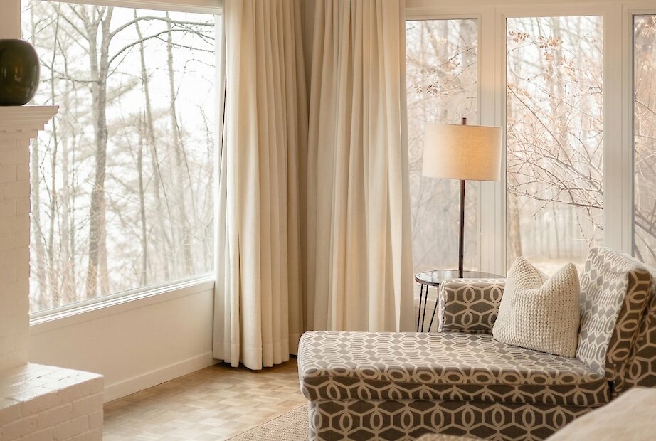 Bright room with large windows, lounge area with chaise, nature views.