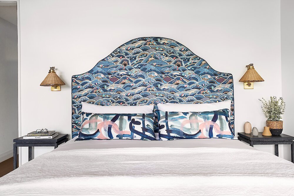 King bed with upholstered headboard in blue wave pattern, paired with decorative pillows and bedside tables.