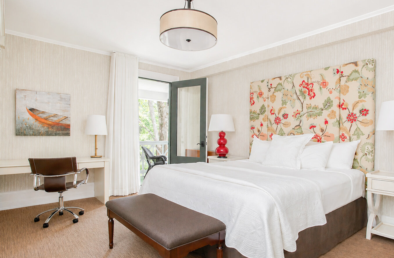Chambre classique lumineuse avec lit king, tête de lit florale, bureau et accès au balcon.