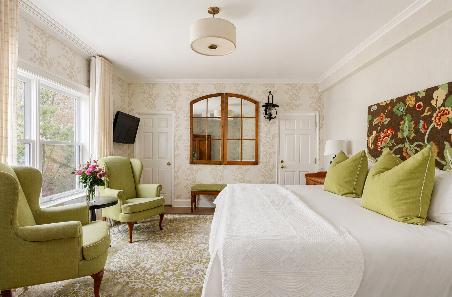 Chambre spacieuse avec lit, coin salon avec fauteuils et lumière naturelle.