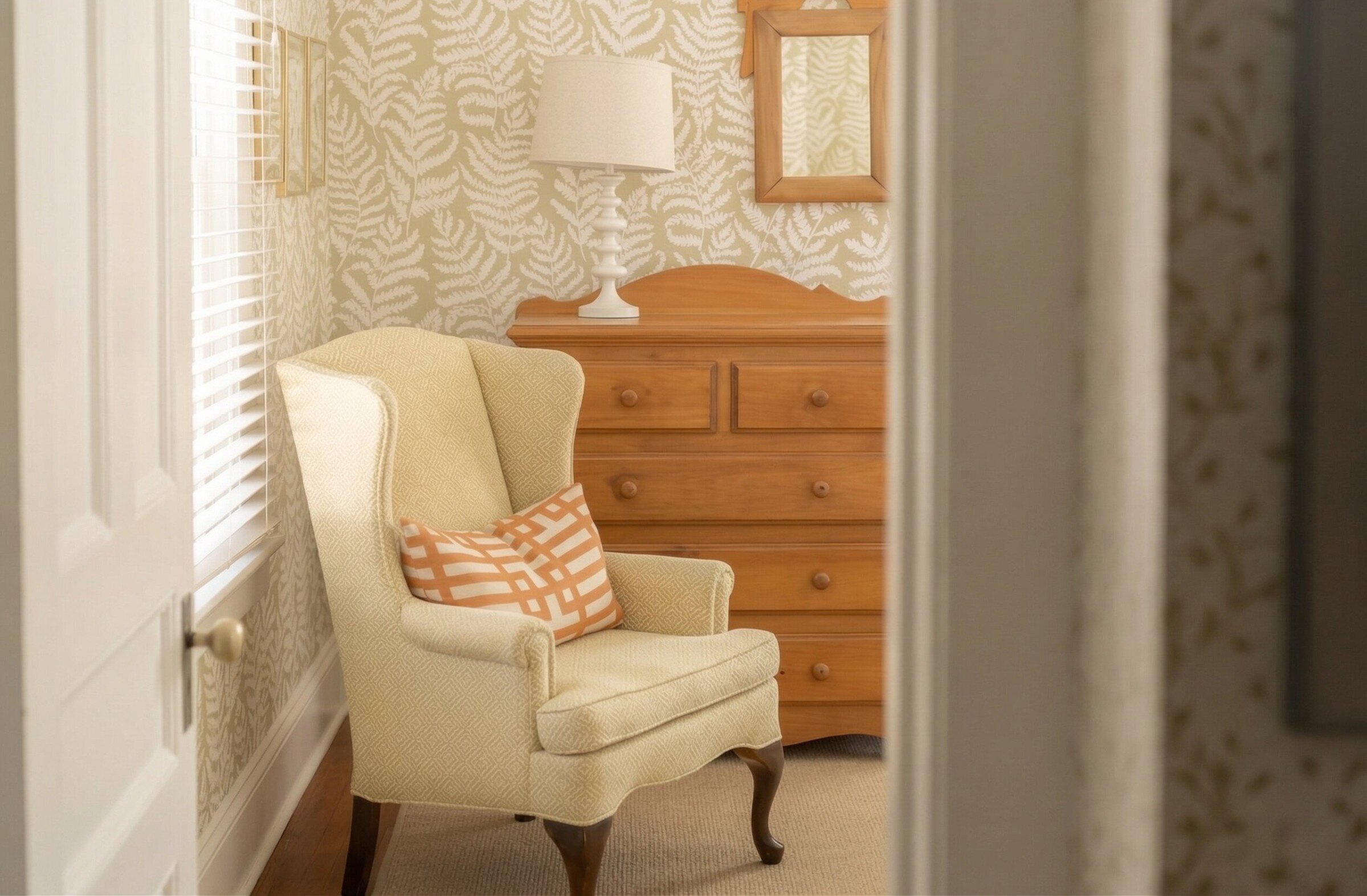 Fauteuil avec coussin près d’une commode en bois et lampe.