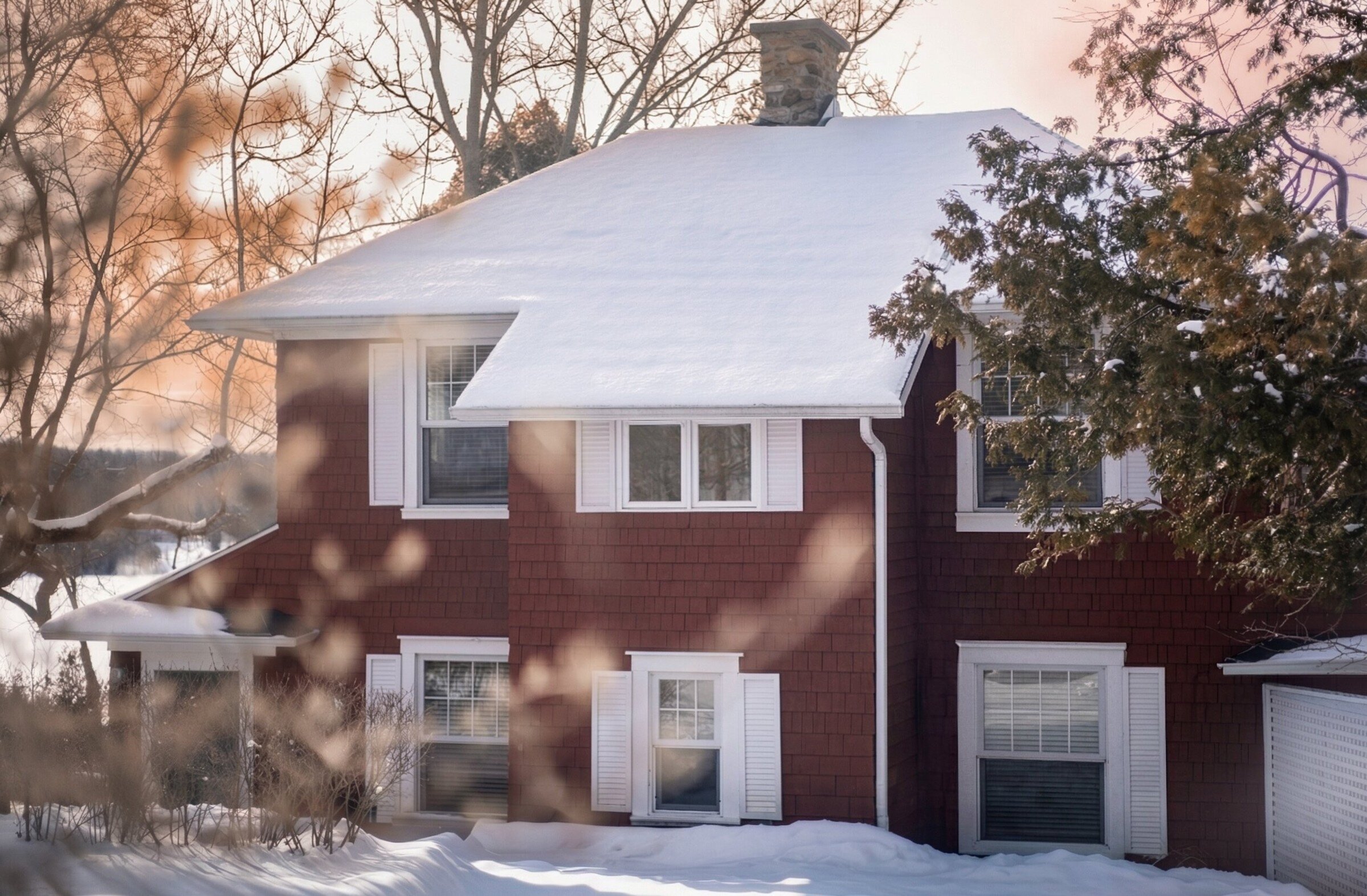 Maison rouge avec toit enneigé et arbres en hiver.