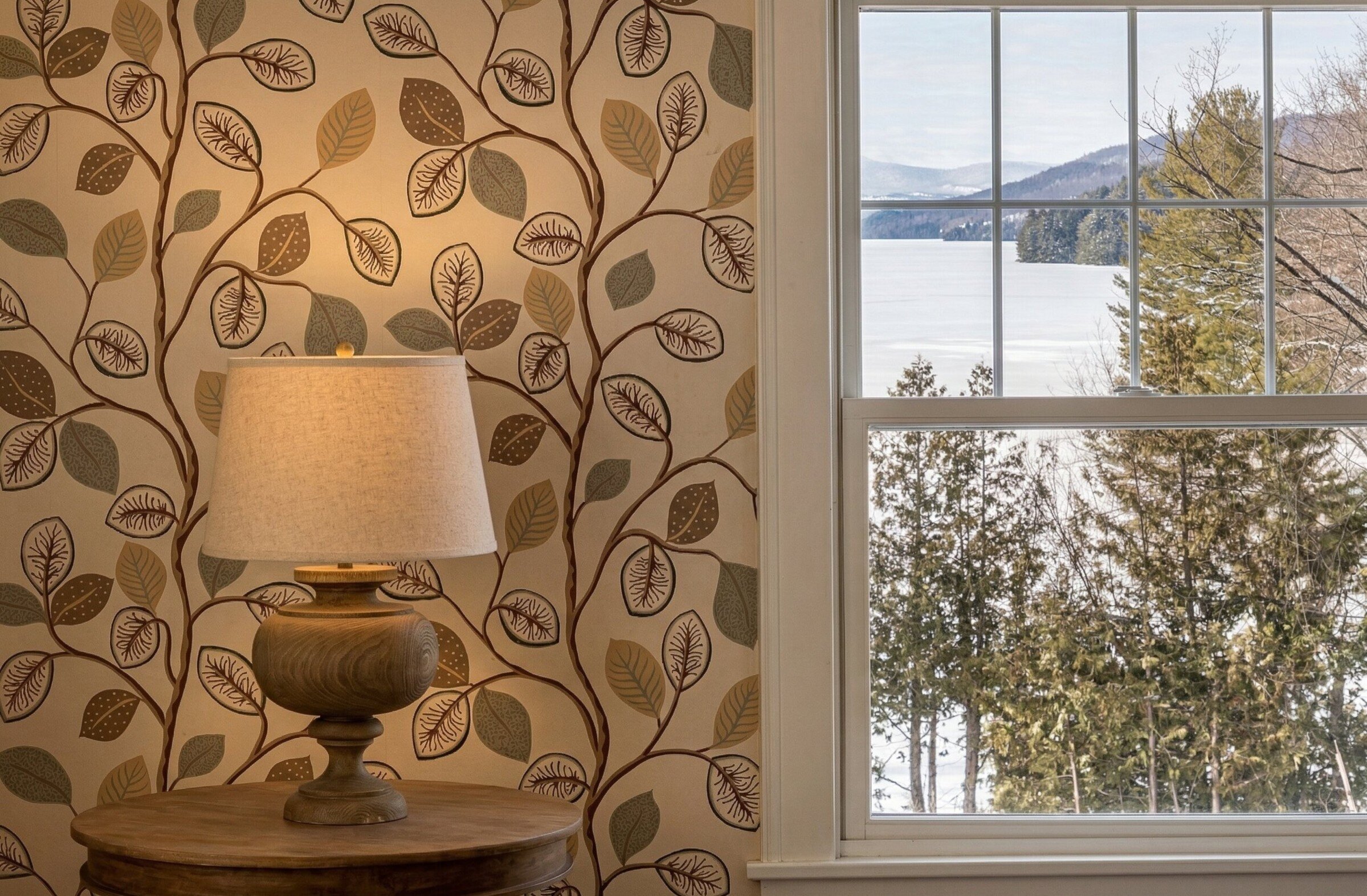 Vue sur un lac avec arbres et montagnes depuis une fenêtre, avec lampe de table.