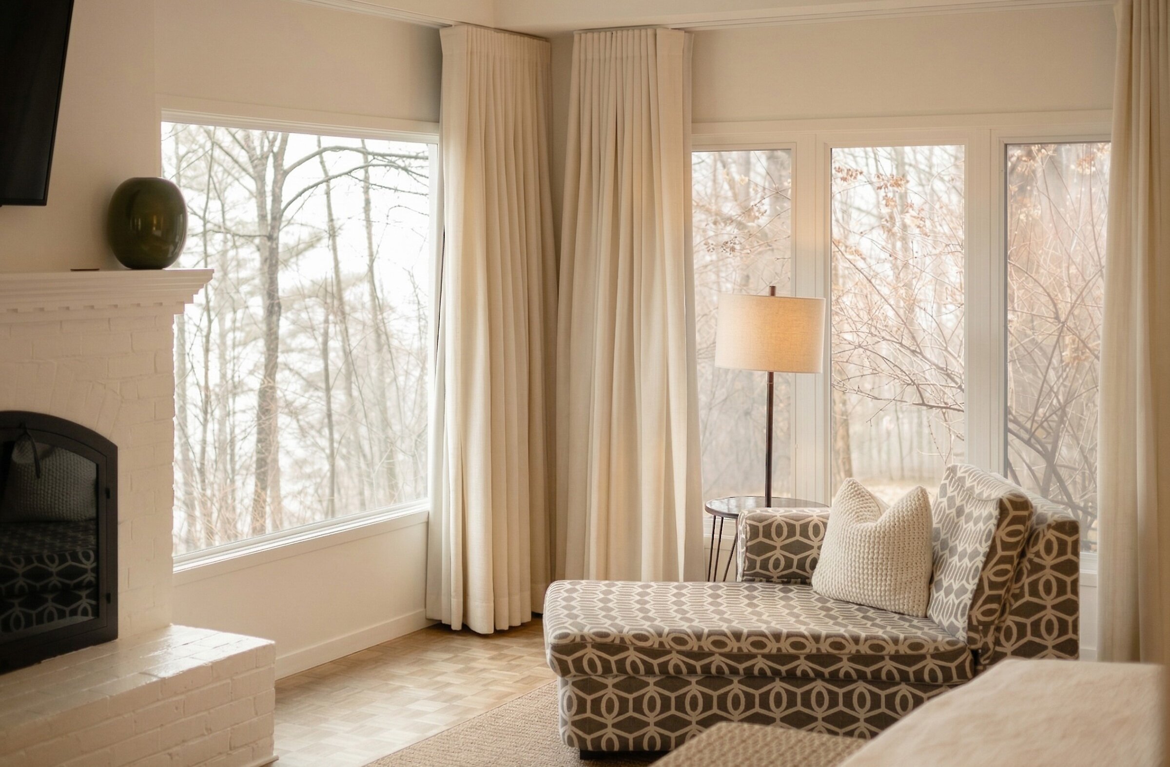 Bright room with large windows, lounge area with chaise, nature views.