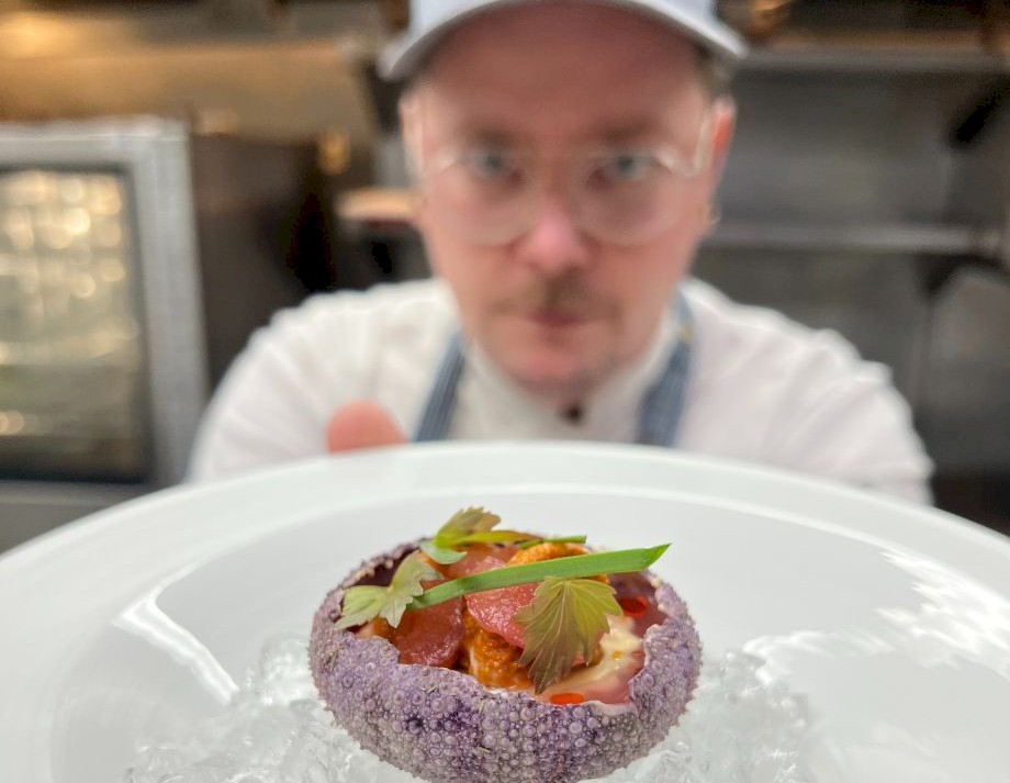 A chef in the kitchen shows off a plate with a sea urchin