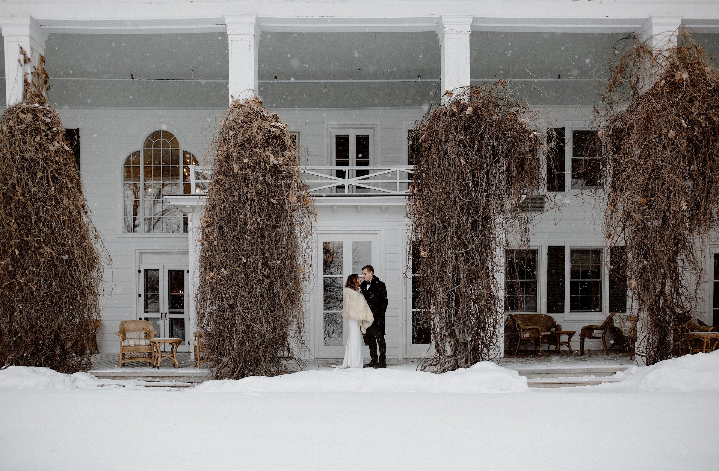 The groom and bride under the snowflakes in front of the Manor