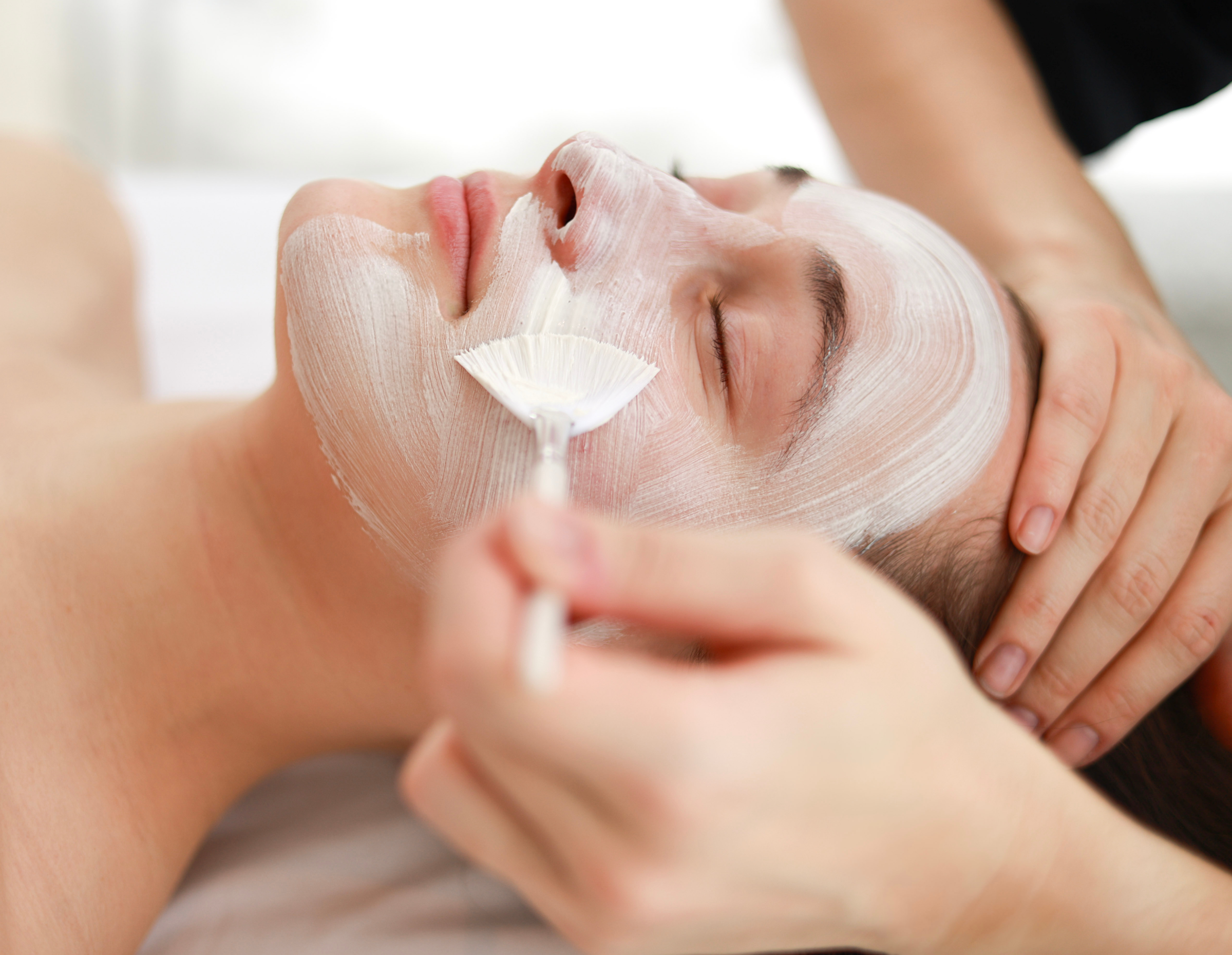 Facial treatment with a mask being applied, eyes closed, in a spa setting.