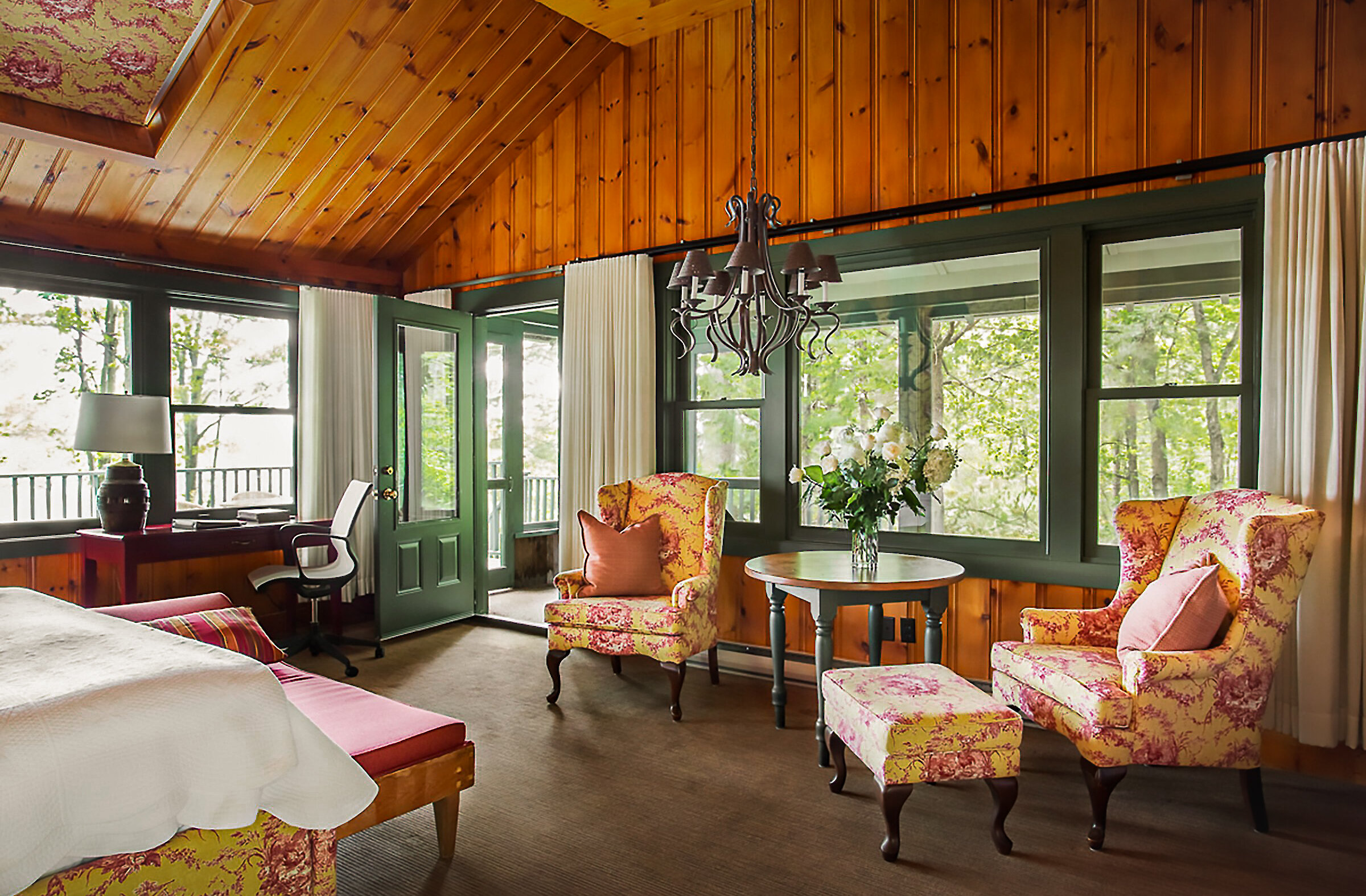 Spacious bedroom with warm wood panelling, cathedral ceiling, sitting area and large windows overlooking the surrounding forest.
