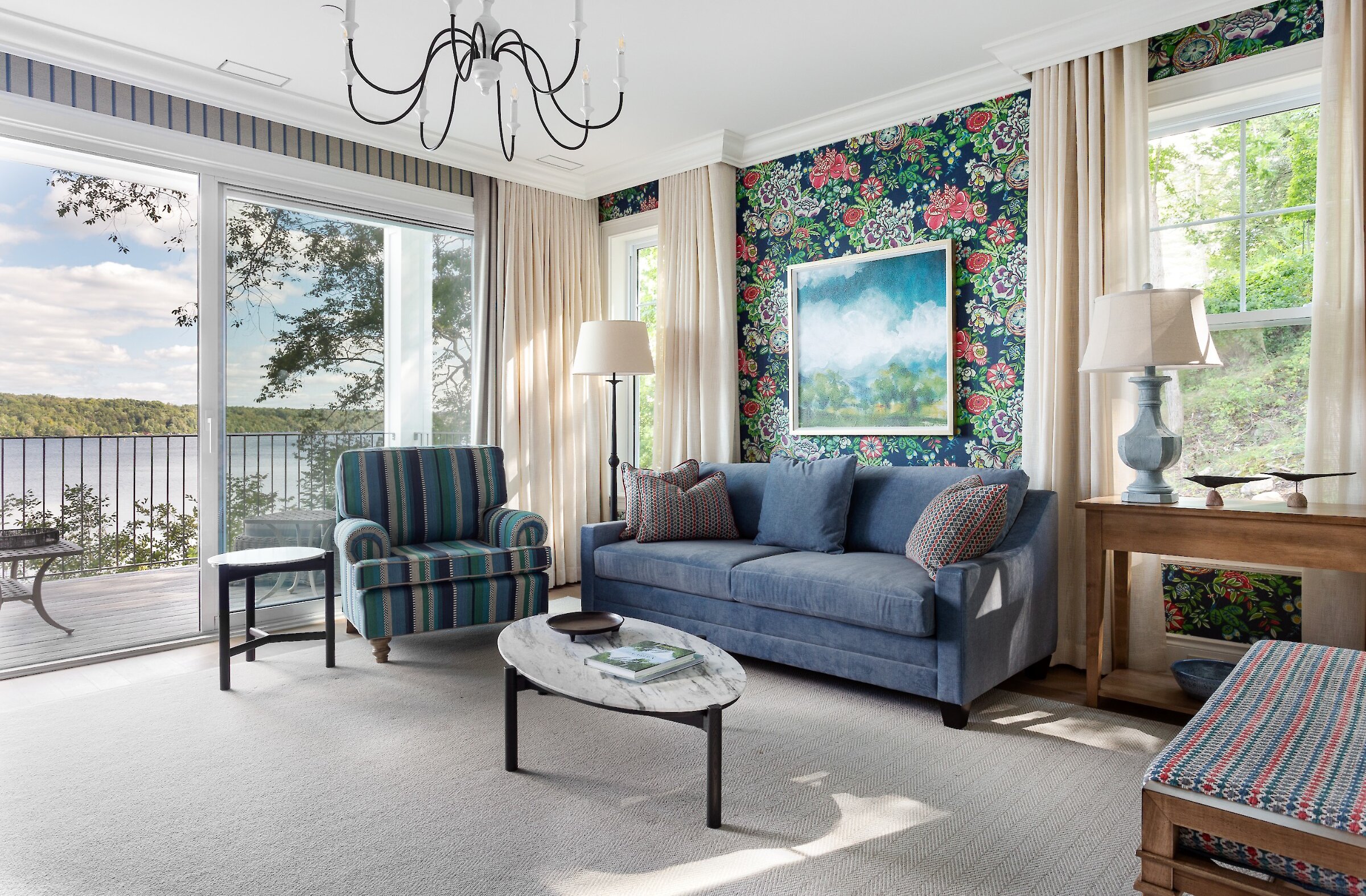 Coin salon lumineux avec canapé bleu, fauteuil, accents floraux et vue sur le lac.