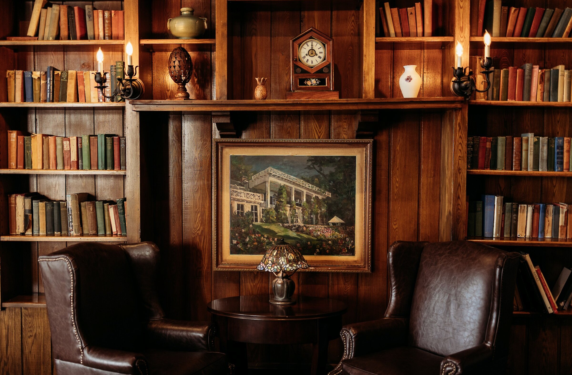 Cozy library lounge with wood-paneled shelves, leather armchairs, and a fireplace surrounded by books.