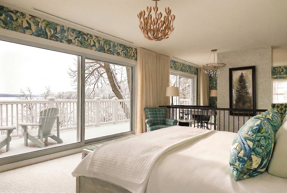 Bright suite featuring a king bed, floor-to-ceiling windows, private balcony, and views over Lake Massawippi. An elegant space combining natural textures, refined furnishings, and abundant light.