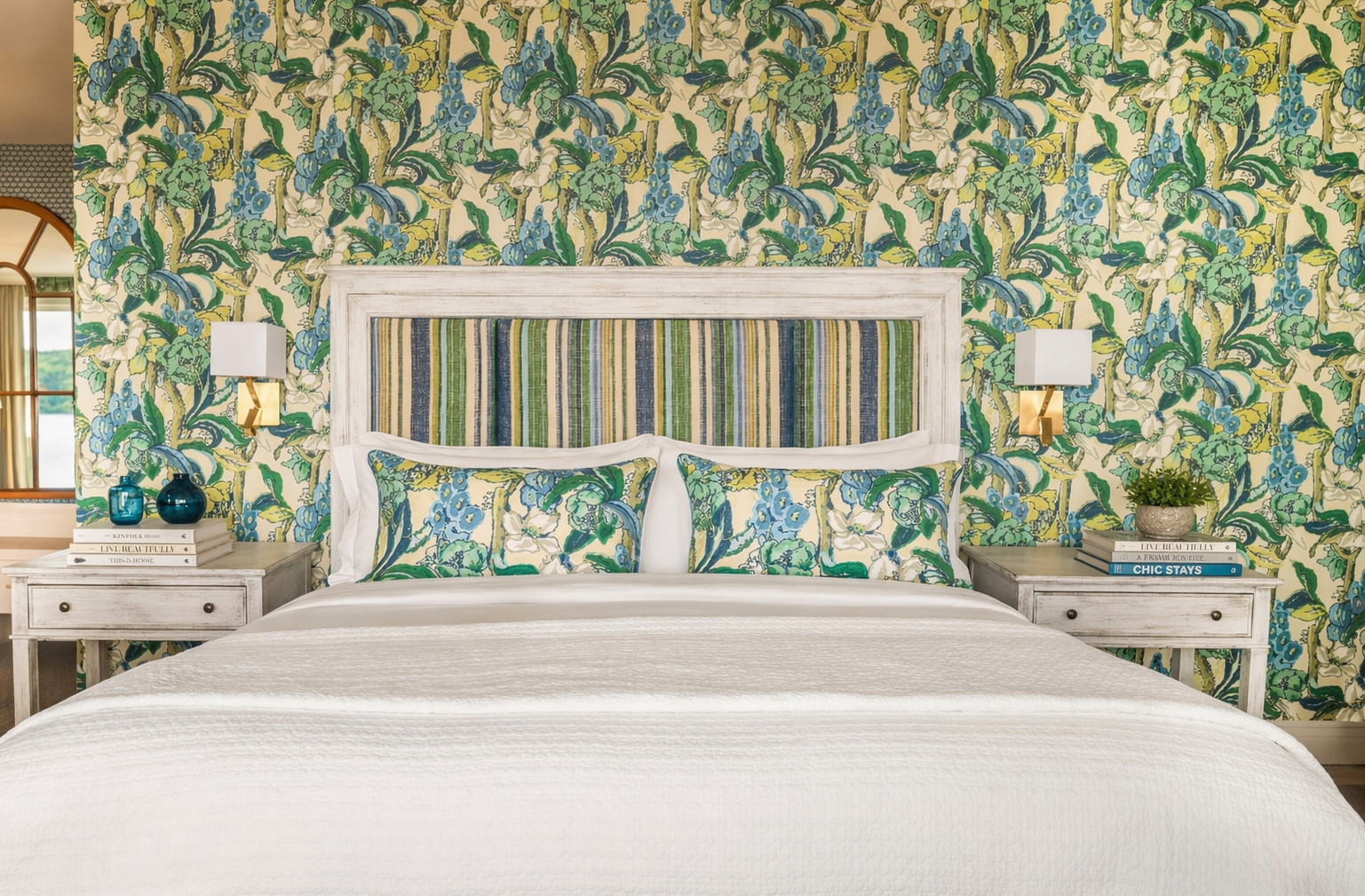 Lit king avec tête de lit rembourrée et linge haut de gamme, encadré par un décor aux motifs botaniques et des tables de chevet élégantes.