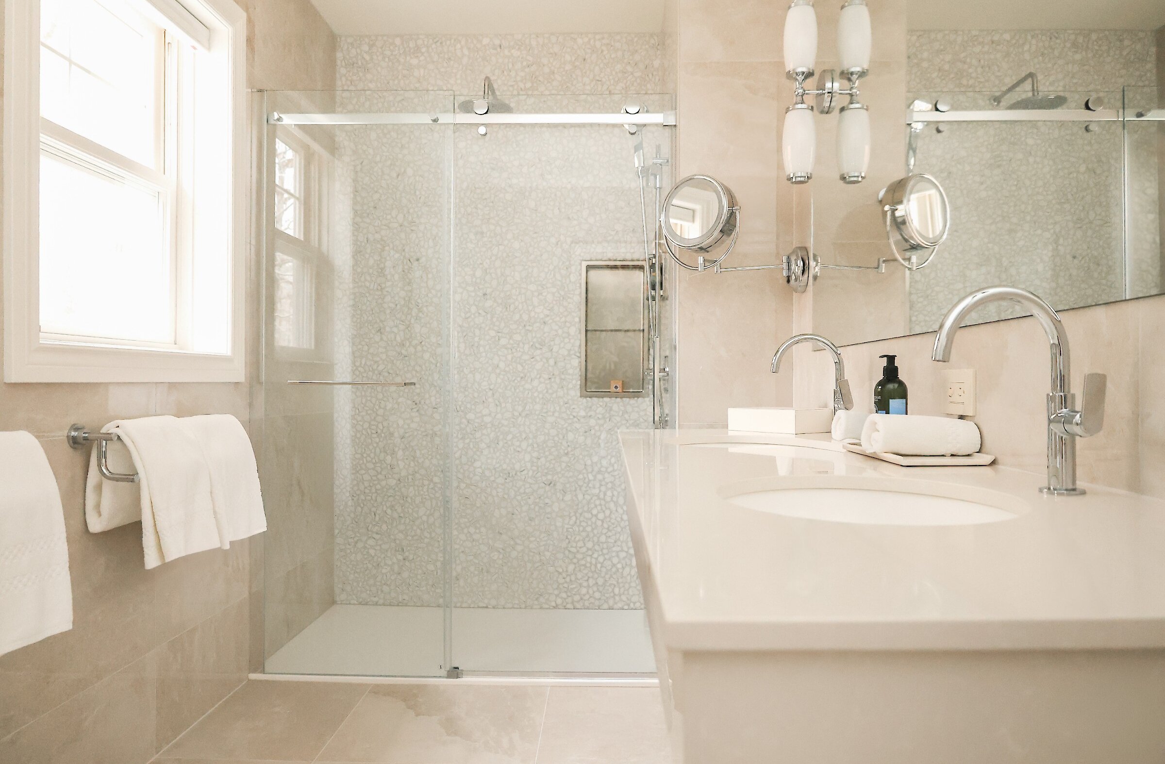 Salle de bain lumineuse avec douche vitrée, double vasque et finitions contemporaines dans des tons neutres et apaisants.