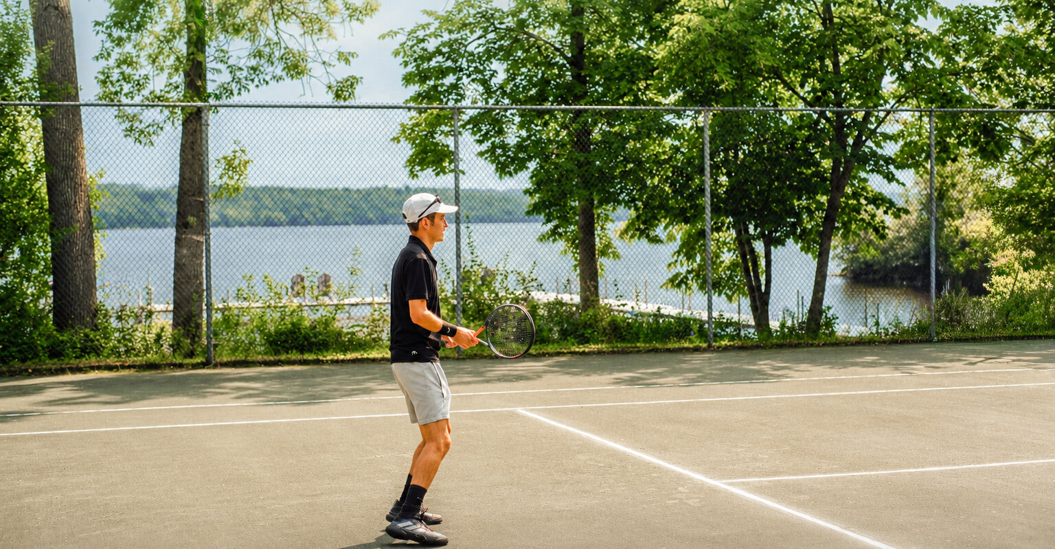 Outdoor tennis court by the lake, surrounded by trees with a view over the water.