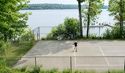 Outdoor tennis court by the lake, surrounded by trees with a view over the water.