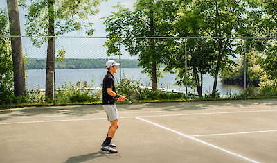 Outdoor tennis court by the lake, surrounded by trees with a view over the water.