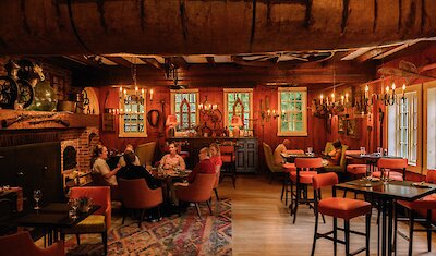 Une salle à manger rustique et chaleureuse, avec des poutres en bois, un éclairage tamisé et une cheminée, créant une atmosphère intime et accueillante.