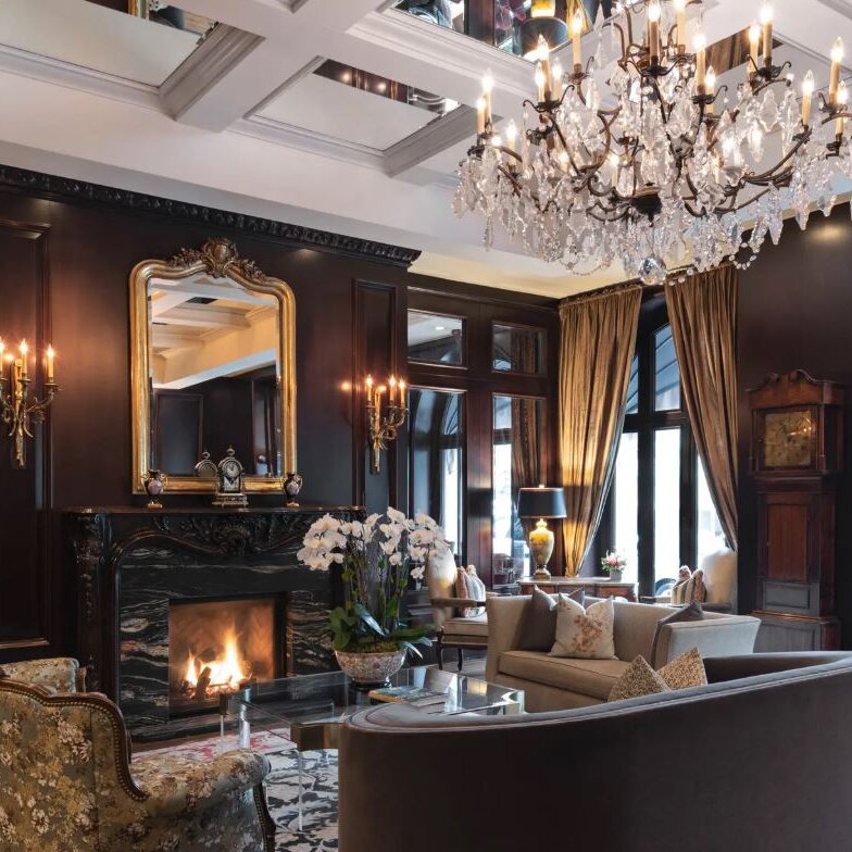 A living room with fireplace, large windows and chandelier